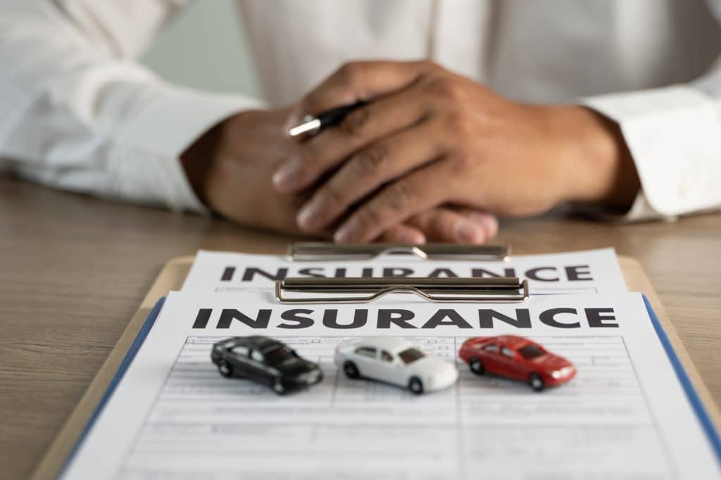 A car insurance policy is on a table with 3 toy cars on top of it